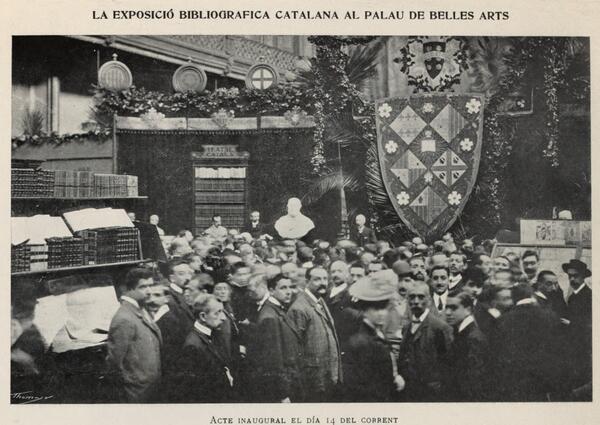 Grup de gent, principalment homes, assistint a la inauguració de l'exposició bibliogràfica de 1906, dins d'un edifici. Amb un pendó a la dreta de la imatge.